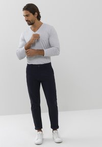 Maglietta grigia a maniche lunghe con scollo a V abbinata a pantaloni chino blu navy e sneaker bianche. I chinos sono arrotolati sui polsini, creando una vestibilità affusolata.