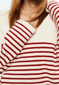 Pull à rayures rouges et blanches avec une texture côtelée, doté de manches longues et d'une encolure décontractée. Le tissu semble doux et décontracté.