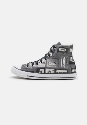 Baskets montantes avec motif de bande cassette noir et blanc, semelle en caoutchouc blanche et lacets noirs sur fond blanc uni.