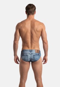 Bañadores tipo slip para hombre en un estampado denim azul claro con un parche de logo, con un diseño ajustado y cobertura mínima trasera.