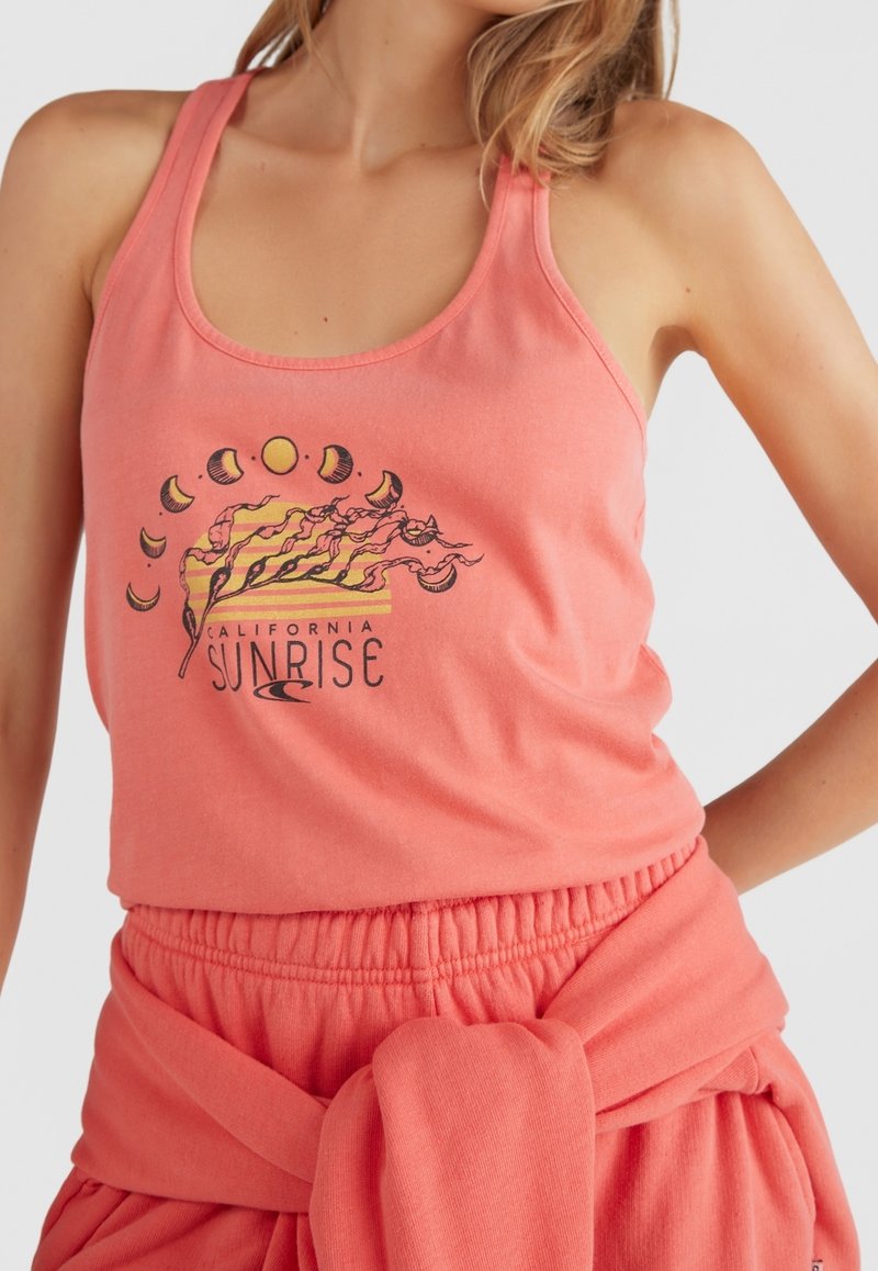 Femme portant un débardeur corail avec un motif lever de soleil en Californie et phases de lune, associé à un pantalon corail assorti et un sweat noué à la taille.