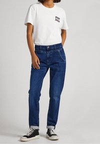 Bílý bavlněný tričko s černým logem "Pepe Jeans", spárované s modrými denimovými džíny. Džíny mají klasický střih s ohrnutými manžetami a dvěma předními kapsami.