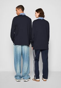 Two individuals wearing long-sleeve navy tops with light blue collars, paired with light blue jeans and dark pants featuring white stripes.