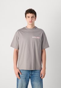 Pilkas medvilnės marškinėliai su apvaliu kaklu ir trumpomis rankovėmis. Kairėje krūtinės pusėje matomas šviesiai rožinis "calvin klein" logotipas. Dėvimi su mėlynomis džinsinėmis kelnėmis.