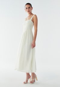 Balta midi kleita ar fakturētu audumu, kvadrātveida izgriezumu, mežģīņu apdari un regulējamām siksnām, kombinēta ar baltām sandales ar siksniņām.