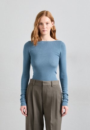 Lys blå, langermet strikket topp med båthals, sammen med høyt liv, grå skreddersydde bukser med folder.