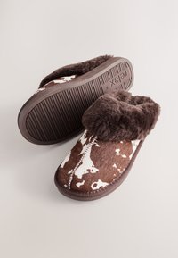 Brązowe kapcie wyściełane futerkiem z wzorem skóry krowy, posiadają miękką górę i teksturowaną gumową podeszwę zapewniającą przyczepność. Zaprojektowane z myślą o wygodzie i ciepłu.