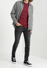 Svart och vit rutig skjorta över en burgundy t-shirt, kombinerat med mörka jeans och svarta sneakers med vita detaljer. Avslappnade designelement.