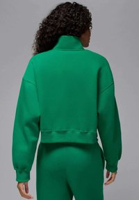 Zielona krótka bluza wykonana z miękkiego materiału, z wysokim kołnierzem, opuszczonymi ramionami i ściągaczami na rękawach. Charakteryzuje się luźnym krojem i minimalistycznym designem.