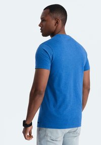 Blå kortärmad t-shirt gjord av mjukt, texturerat tyg. Har en klassisk rundad halsringning och ett märke på nedre vänstra sidan.