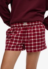 Czerwono-białe kraciaste szorty z flaneli z elastycznym pasem i naszywką, o luźnym kroju i miękkiej fakturze.