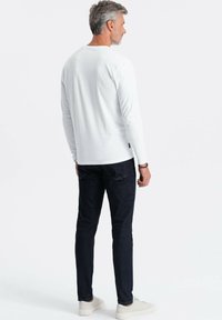 Weiße Langarmbluse kombiniert mit dunkelblauen Jeans. Die Bluse hat einen runden Halsausschnitt und die Jeans haben einen figurbetonten Schnitt. Weißes Casual-Sneaker rundet den Look ab.
