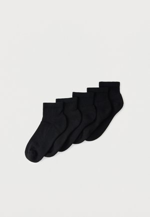 Sechs Paare schlichte schwarze Knöchelsocken in einer ordentlichen Reihe auf hellem Hintergrund angeordnet.