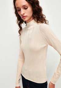 Beige gerippter Pullover mit hohem Kragen und langen Ärmeln, ausgestattet mit vertikalen Streifen und einer weichen Stricktextur.