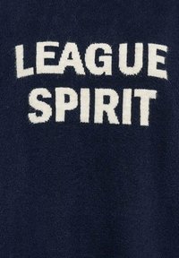 Donkerblauwe tekst met de woorden "LEAGUE SPIRIT" in grote, crèmekleurige letters op een zachte, gestructureerde stofachtergrond.