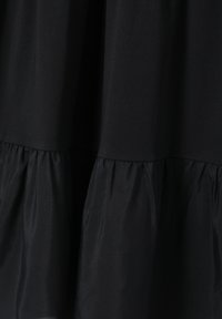 Black dress featuring a smooth, fitted top and a textured, tiered skirt. Material appears soft with a slight sheen.