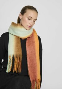 Écharpe en laine présentant des couleurs dégradées allant du bleu clair au brun et à l'orange, avec des extrémités frangées et une apparence douce et texturée.
