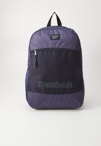 Reebok kuprinė tamsiai violetinės ir juodos spalvos audinyje, su viršutiniu rankenom, priekinėmis užtrauktukinėmis kišenėmis ir logotipu apatinėje priekinėje dalyje. Lengvas dizainas.