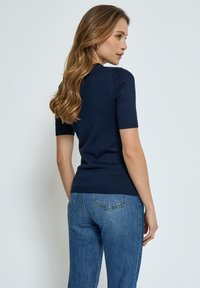 Mörkblå kortärmad tröja med ribbat halsband och nederkant, tillverkad av ett slätt material, i kombination med ljusblå denimjeans.