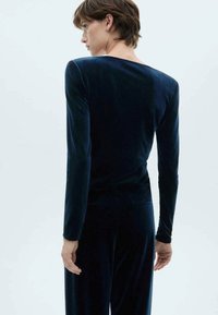 Marineblauwe fluwelen bodysuit met lange mouwen, met een strakke design, aansluitende silhouet en een gladde, zachte textuur.