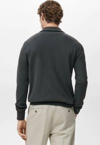 Pull-over gris foncé texturé avec col et manches longues, assorti à un pantalon de couleur claire avec poches arrière et détails à boutons.