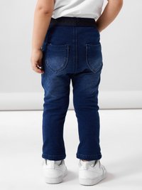 Σκούρες μπλέ τζιν παντελόνες με slim fit, που διαθέτουν δύο πίσω τσέπες. Συνδυάζονται με λευκά αθλητικά παπούτσια και έχουν ελαστική μέση για άνεση.