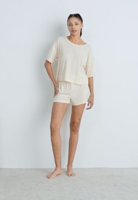 Beige loungewear szett, rövid ujjú felsővel és hozzá illő sorttal, puha anyagból készült, laza szabású. Egyszerű és letisztult dizájn.