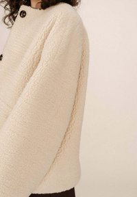 Giacca in pile di colore crema con una texture morbida, dotata di colletto rotondo, due bottoni e una vestibilità comoda, che mette in mostra un design semplice e minimale.