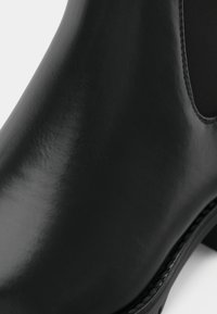 Gros plan d'une botte cheville en cuir noir lisse avec panneau latéral élastique et petit talon empilé.