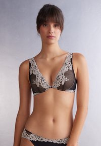 Zwarte kanten beha met een delicate beige bloemenprint, met een diep uitgesneden decolleté en brede kanten schouderbanden. Gecombineerd met bijpassende zwarte slips met kanten accenten.