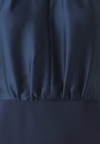 Morska haljina s glatkim satenskim gornjim dijelom i teksturiranim donjim dijelom, s nabranim pojasom i lepršavim siluetom.