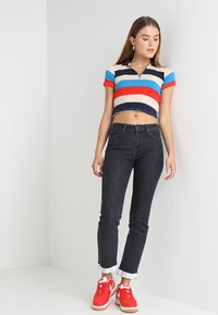 Camisa polo corta con rayas rojas, azules y marinas; combinada con jeans negros de talle alto y zapatillas rojas con detalles en blanco.