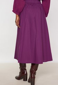 Gonna midi viola con vita arricciata, realizzata in tessuto morbido, abbinata a stivali al ginocchio in pelle marrone con tacco.