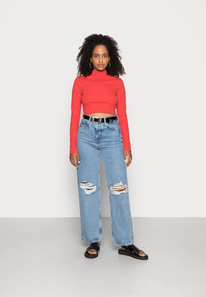 Suéter curto de gola alta vermelho, jeans rasgados de cintura alta azul claro, cinto preto e sandálias pretas. Tecido suave e corte descontraído com detalhes desgastados.