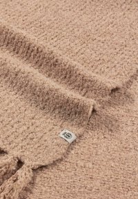 Textured, light pink blanket with a soft, fuzzy finish; features a label on the edge, fringes at one end, and a woven pattern.