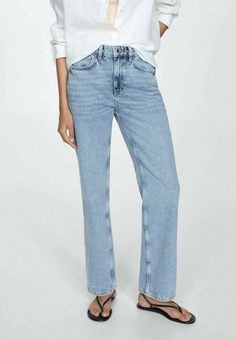 Jeans de pierna recta de color azul claro, hechos de denim, con una cintura alta y bolsillos delanteros, combinados con chanclas negras y una camisa blanca.