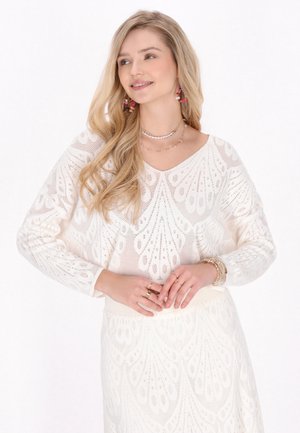 Haut en tricot blanc à manches longues avec un col en V et un motif en dentelle complexe, assorti d'une jupe correspondante présentant un design texturé.