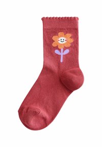 Chaussette en coton rouge avec un bord supérieur festonné, arborant un motif de fleur souriante en orange et violet sur le côté. Texture lisse.
