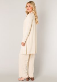 Beige lange mouw tuniek met een losse pasvorm, gecombineerd met crèmekleurige broek met brede pijpen. Soepele textuur, eenvoudig ontwerp en subtiele val.