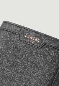 Portafoglio in pelle nera testurizzata con motivo impresso e logo "LANCEL PARIS" in tono dorato nella parte superiore. Presenta linee pulite e un design minimalista.