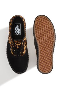 Par de zapatos Vans de caña baja con puntera de ante negro y tejido con estampado de leopardo, uno mostrando la vista superior y el otro mostrando la suela con patrón de gofre.