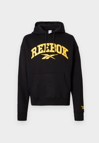 Čierna mikina s kapucňou vyrobená z bavlny, s žltým logom "REEBOK" na hrudi, s šnúrkou na kapucni a prednou vreckom. Žebrované manžety a spodný lem.