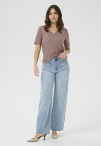 Top corto de manga corta en mauve claro con canalé y cuello en V, combinado con jeans de mezclilla azules de pierna ancha y tacones de punta beige. Diseño simple y contemporáneo.