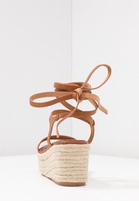 Brun läder kilsandaler med en plattform i rep-textur, utsmyckade med korsande remmar och ankelsnören. Barfotadelen syns på sulan.
