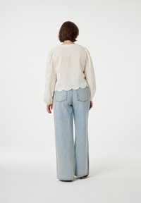 Lichte crèmekleurige blouse met opgezette mouwen en gegolfde zoom, gecombineerd met lichtblauwe wijde jeans. Zachte stof met minimale details.