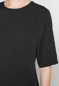 Černý krátký rukáv top s kulatým výstřihem, hladkou texturou a minimalistickým designem s jemnými švy na švech.