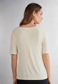 Cremefarvet t-shirt med korte ærmer og bred udskæring. Blød tekstur, afslappet pasform og minimalistisk design, velegnet til hverdag.