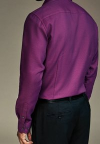 Man in een gemêleerde paarse lange mouw shirt, ingestopt in zwarte broek met een zwarte riem, weergegeven van achter en opzij.