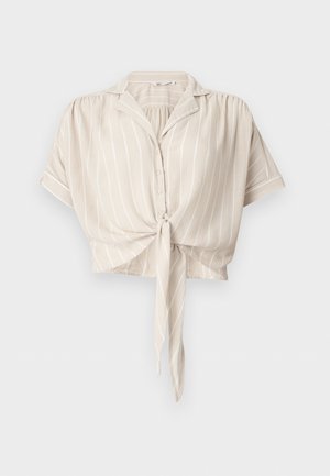 Μπεζ μπλούζα με κοντά μανίκια και λευκές κάθετες ρίγες, κουμπιά μπροστά, γιακάς και δέσιμο μπροστά στη μέση.