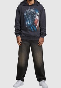 Donkergrijze hoodie met een grafische print van een stekelig object, gecombineerd met losse donkere jeans en witte sneakers.